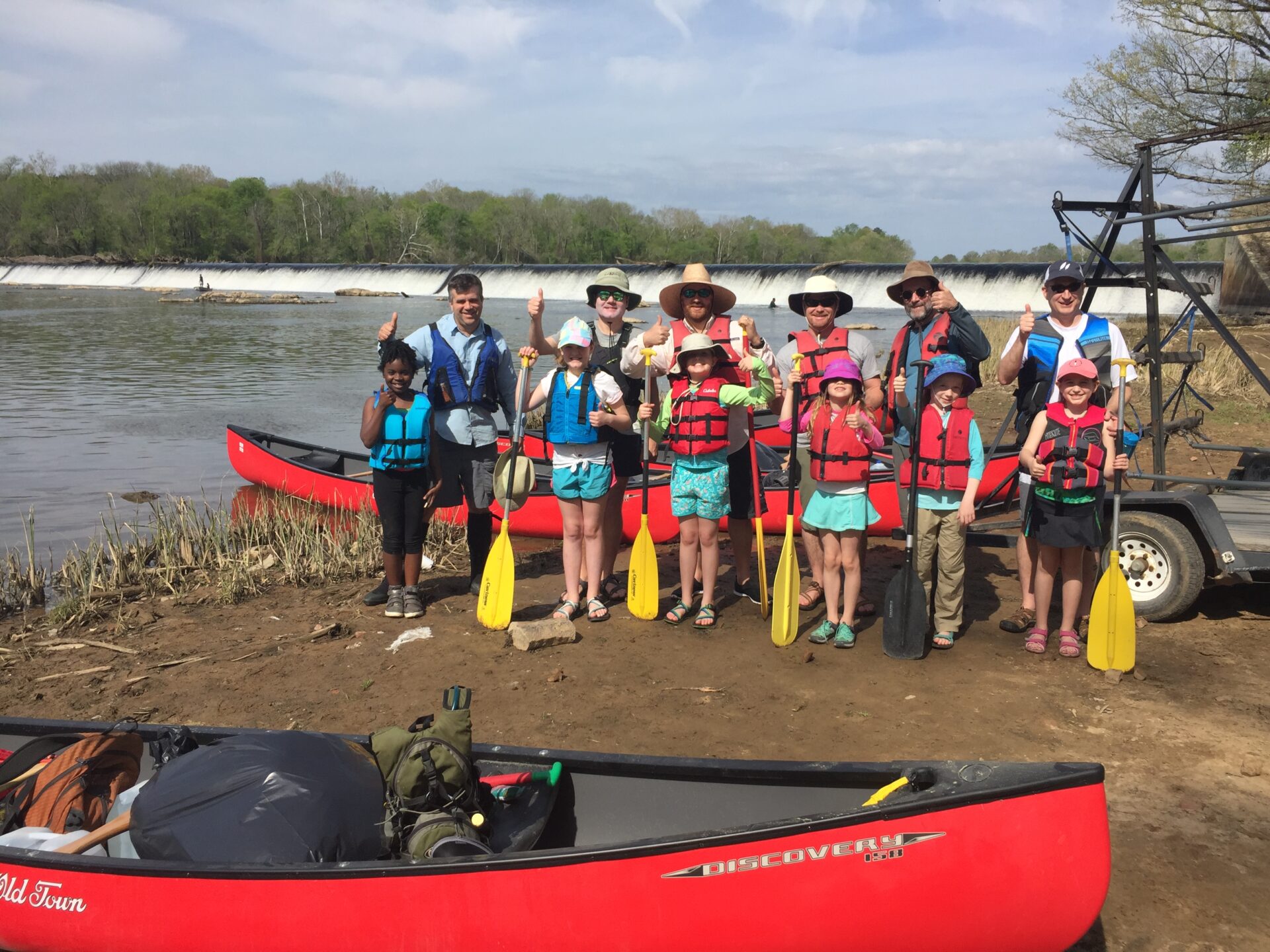 A group of children and adult chaperones, canoes, with Buckhorn Dam in background.